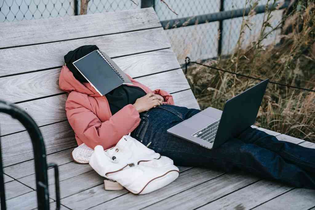 Человек лежит с компьютером на коленях и с блокнотом на лице